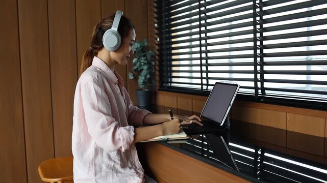 Young female student smiling while studying at desk with laptop and books, engaged in research, e-learning, and university coursework indoors.
 - Powered by Adobe