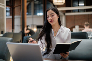 Focused businesswoman working on laptop and taking notes in notebook in coworking space