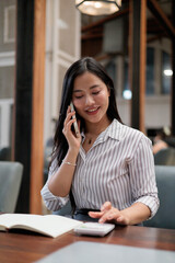 Businesswoman using calculator and talking on smartphone at office desk