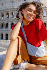 A cheerful and lively young woman joyfully poses by the magnificent Colosseum, showcasing her vibrant and colorful style while capturing the enchanting beauty of Rome along with its rich culture