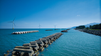 残暑の中の日本の富山県東部の海岸線で発電をしている洋上風力発電風車の様子