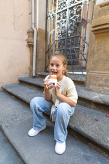In a charming urban environment, a joyful little child is seated on the stairs, happily munching on a tasty snack, their expressions radiating pure delight and innocence in the warm sunlight
