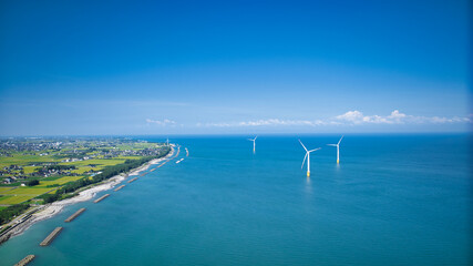 残暑の中の日本の富山県東部の海岸線で発電をしている洋上風力発電風車の様子