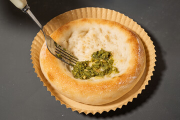 A Freshly Baked Bread Bowl Filled with Vibrant Green Pesto, Served on a Paper Tray with a Fork Ready for Enjoyment
