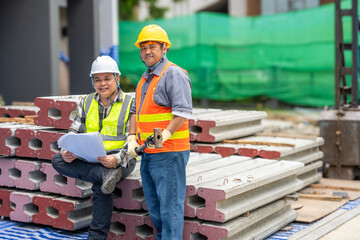 Two construction workers wea safety helmets and reflective vests standing outdoors at a construction site with bricks and safety equipment, discussing project plans