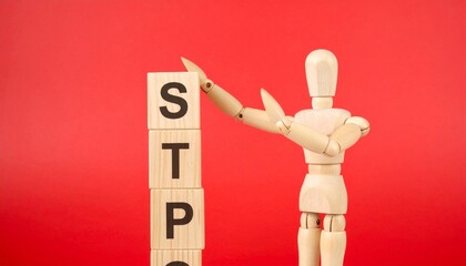 Wooden mannequin points to stacked blocks spelling “STOP” against red backdrop. A symbolic gesture of pause, warning, or reflection—blending visual clarity with emotional intent.