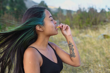 Young woman with vibrant, colorful hair and a tattoo enjoying a delicious nacho chip outdoors