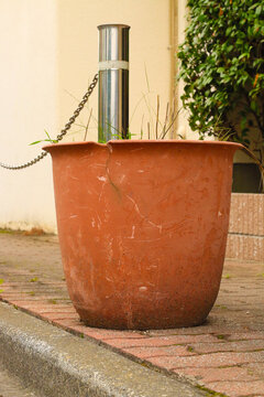 Close-up of a cracked terracotta planter on a sidewalk with grass growing inside. Urban detail showing texture, decay, and resilience of nature in a city environment.