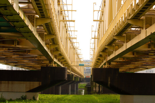 Symmetrical view under a large steel bridge with strong beams and supports. Industrial architecture detail showing perspective, structure, and urban engineering.