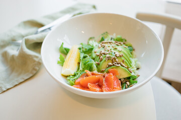 Bowl with green salad with smoked salmon, lettuce and avocado, garnished with seeds and lemon.