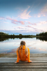 Fototapeta premium Woman relaxing at the lake bridge travel solo in Finland, girl enjoying sunset landscape travel lifestyle outdoor autumn vacations trip in the wild sustainable tourism freedom adventure exploration