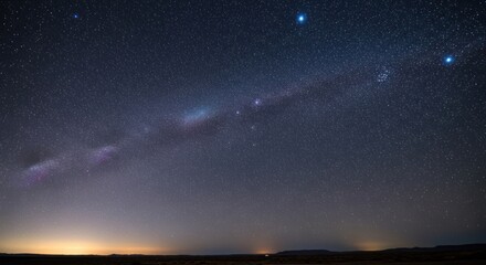 Milky Way stretches across night sky, city lights glow on horizon below