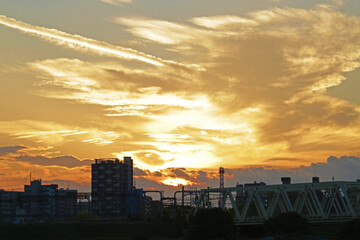 Dramatic sunset sky over city skyline with bridge silhouette. Golden clouds and warm evening light create a striking urban landscape.