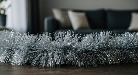 Silver tinsel garland lays on wood surface, blurred room background