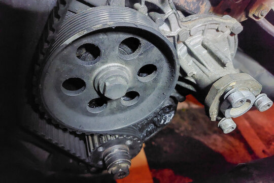 Close-up view of an intermediate shaft pulley and belt in a diesel engine, showcasing worn teeth and a robust pulley design, essential for power transmission in heavy machinery.