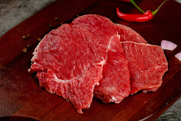 Fresh Raw Beef Steaks on Wooden Cutting Board with Red Chili Peppers