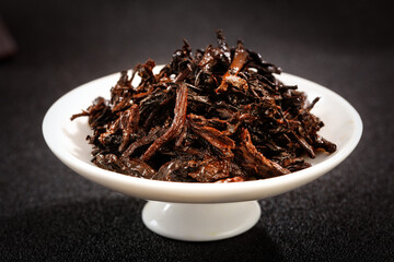 Traditional Chinese Puerh Tea Cake Broken into Dark Fermented Leaves on White Plate
