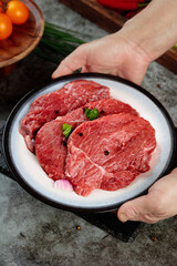 Fresh Raw Beef Steaks on Plate Held by Hands Ready for Cooking with Herbs and Vegetables