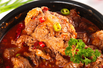 Spicy Braised Beef Oxtail Stew with Peppers and Fresh Herbs in Traditional Black Bowl