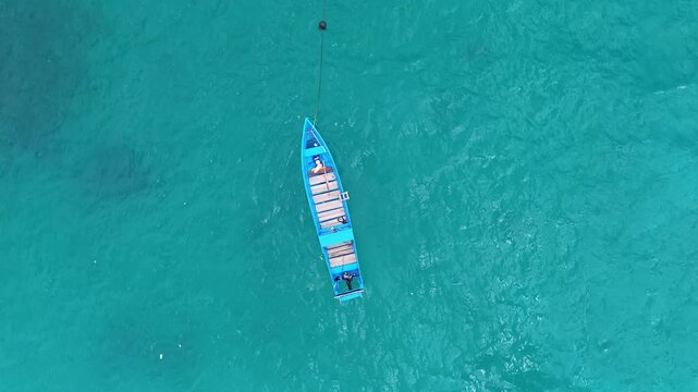 Drone view of an empty blue wooden boat anchored on turquoise sea, parked and floating peacefully on clear water.