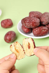 Dried Jujube Dates from Xinjiang China - Hands Showing Cut Fruit Interior with Bowl of Whole Red Dates on Green Background
