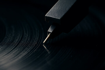 Macro shot of a turntable needle touching vinyl grooves, highlighting textures, retro aesthetics, and analog audio precision in dark tones.
