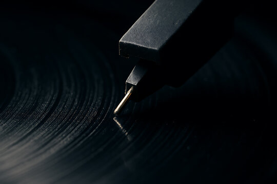 Macro shot of a turntable needle touching vinyl grooves, highlighting textures, retro aesthetics, and analog audio precision in dark tones. - Powered by Adobe