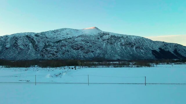 This drone footage capturing the serene winter landscape near Bud Fishing Village in Norway, featuring snow covered mountains, a vast expanse of snow, and a clear sky, ideal for showcasing natural bea