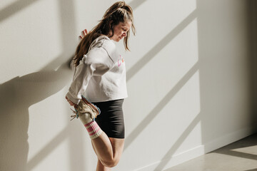 Woman in sneakers and shorts stretches body using wall for support