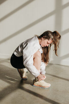 Woman in biker shorts and sweatshirt bends down to tie shoes