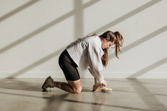 Woman in biker shorts and sweatshirt bends down to tie shoes