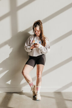 Woman leans against wall while using phone light streams in around her