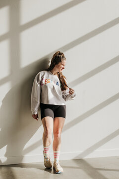 Smiling woman leans against wall while light streams in around her