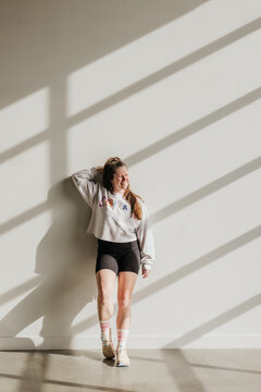 Smiling woman leans against wall while light streams in around her