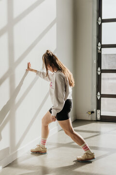 Woman in sneakers and shorts stretches body using wall for support