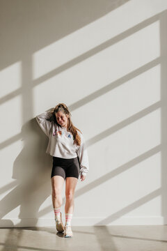 Smiling woman leans against wall while light streams in around her