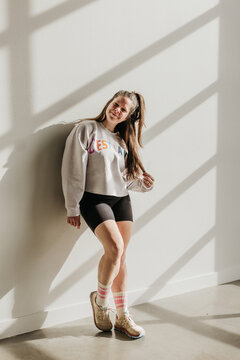Smiling woman leans against wall while light streams in around her