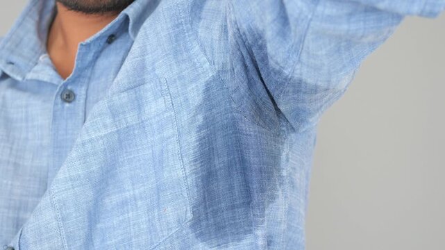 A man is showing noticeable underarm sweat stains on his blue shirt
