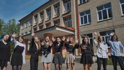 Happy students waving in front of the school building, celebrating unity and achievements on a sunny day