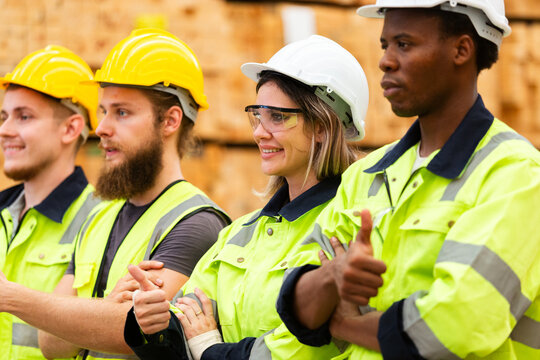 Confident warehouse workers in high visibility safety gear with crossed arms, standing in lumber storage facility, representing unity, professionalism, and industrial team motivation.
