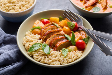 Tender roast duck in delicious red curry with potatoes and tomatoes on brown rice, ready to eat