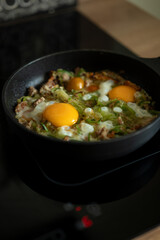 Cooking scrambled eggs with vegetables in a black skillet on a stovetop in a warm kitchen setting