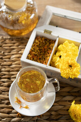 Herbal tea served in a clear glass cup with yellow flowers and dried herbs on a bamboo mat