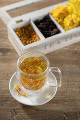 Warm herbal tea served in a glass cup with dried flowers and spices arranged in a wooden box