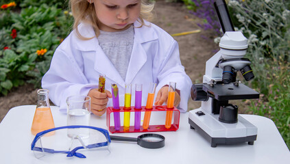 A little girl conducts experiments using test tubes, reagents, and a microscope.