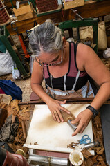 Female cigar artisan pressing tobacco leaves with metallic tool while crafting premium handmade habanos in traditional cuban factory workshop