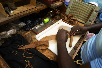 Skilled cigar maker rolling habano using traditional tools, working with dried tobacco leaves...