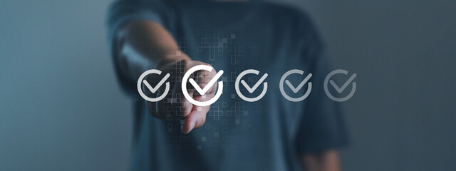 Hand pointing at digital check mark or checklist, online assessment, survey response, multiple choice exam, evaluation, questionnaire, and answer selection. Digital survey and evaluation concept.
