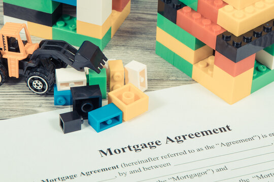 Houses made of toy blocks, miniature excavator and mortgage agreement form. Financing building or purchase of real estate - Powered by Adobe