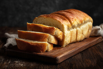 Sliced bread on a dark wooden board with a knife and cloth, ideal for rustic food blogs or bakery menus, or food packaging designs.